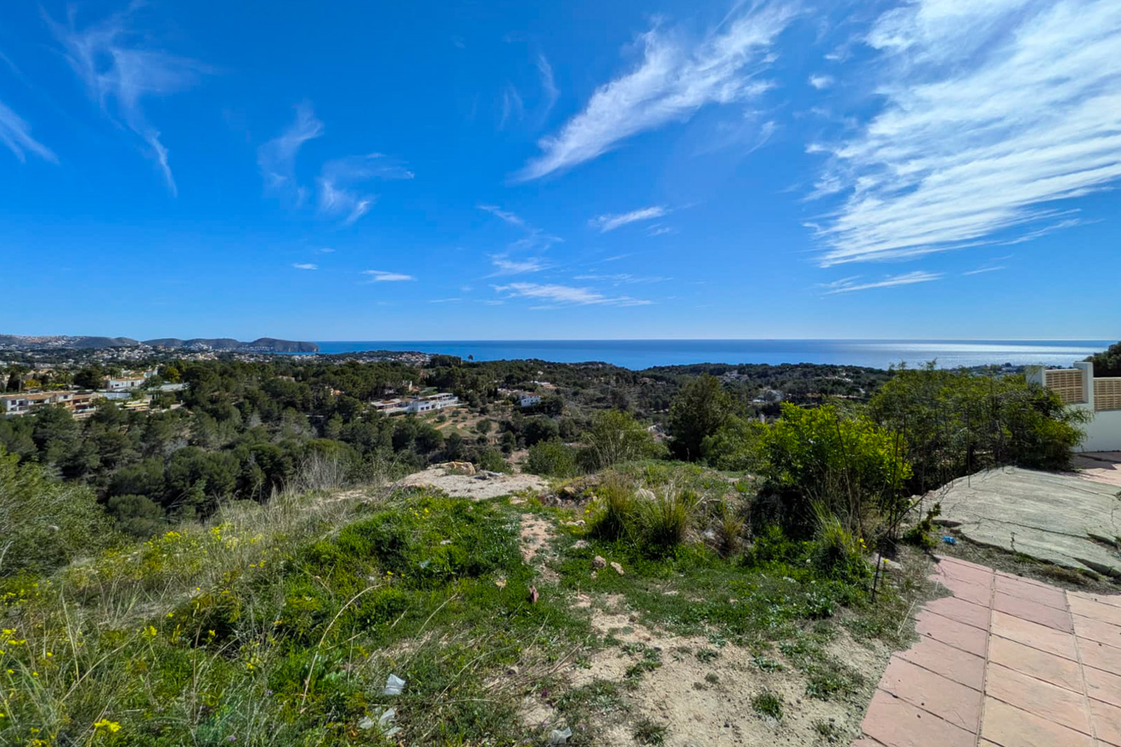 Vista panorámica desde la parcela elevada en Benissa, mostrando la costa mediterránea, el Cap D'or y colinas arboladas bajo un cielo despejado.