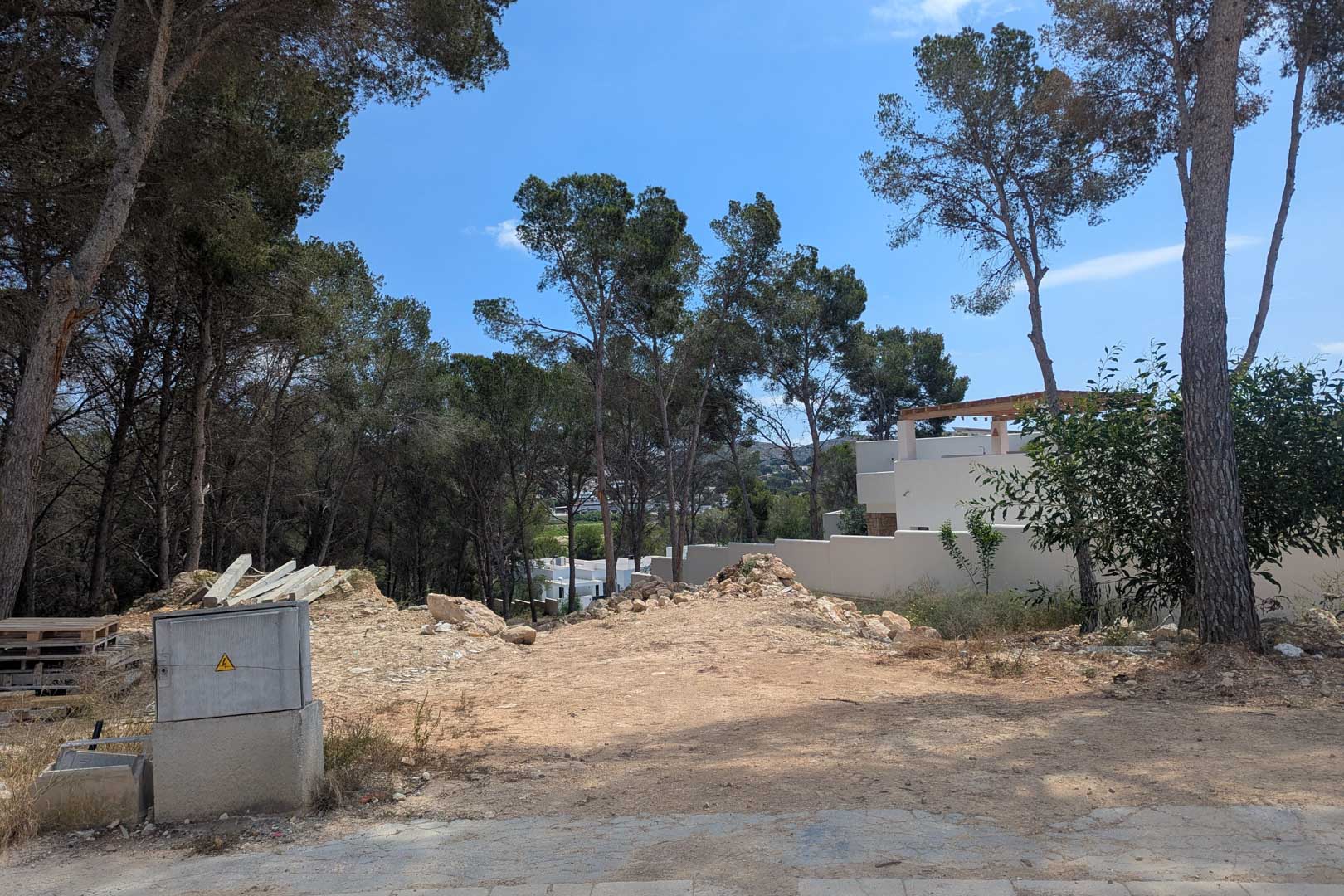 Parcela elevada rodeada de pinos maduros en Moraira, con terreno despejado y acometidas preparadas para el inicio inmediato de la construcción de la villa.