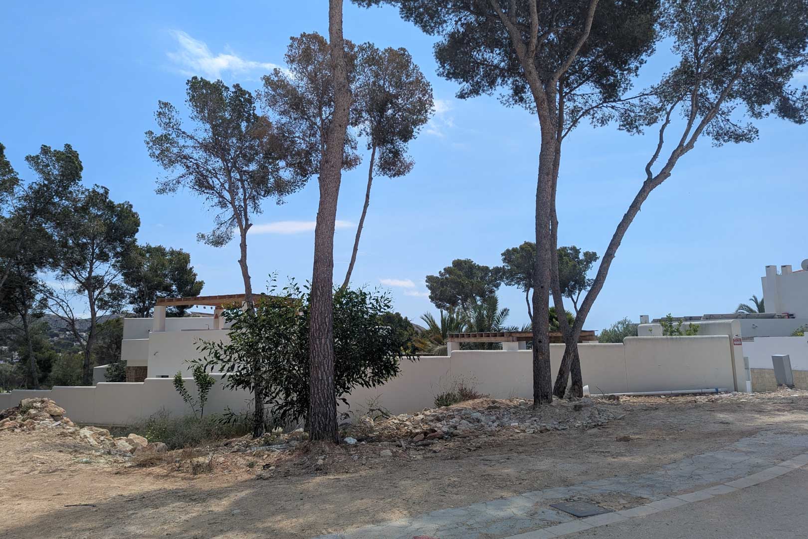 Vista de la parcela con pinos maduros y muros perimetrales blancos, lista para el inicio del proyecto de villa de estilo ibicenco en Moraira.