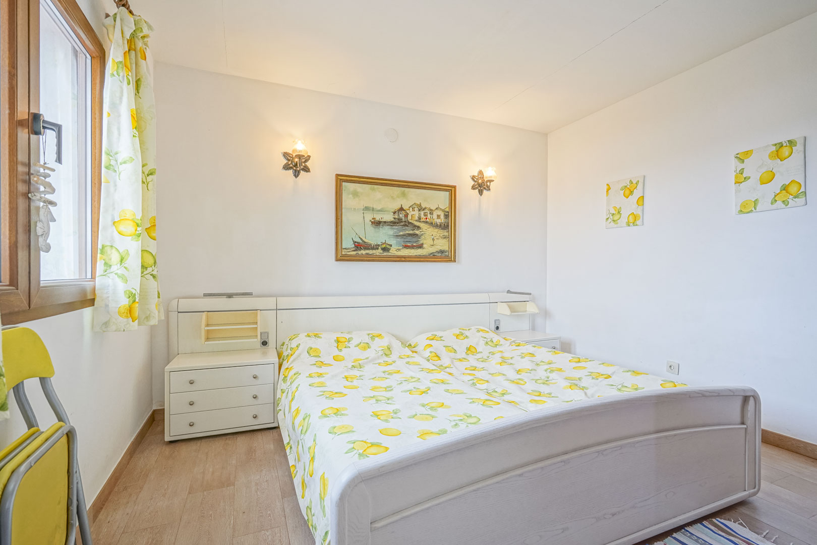 Dormitorio luminoso con cama doble, cabecero blanco con mesitas de noche integradas y decoración de temática de limón.