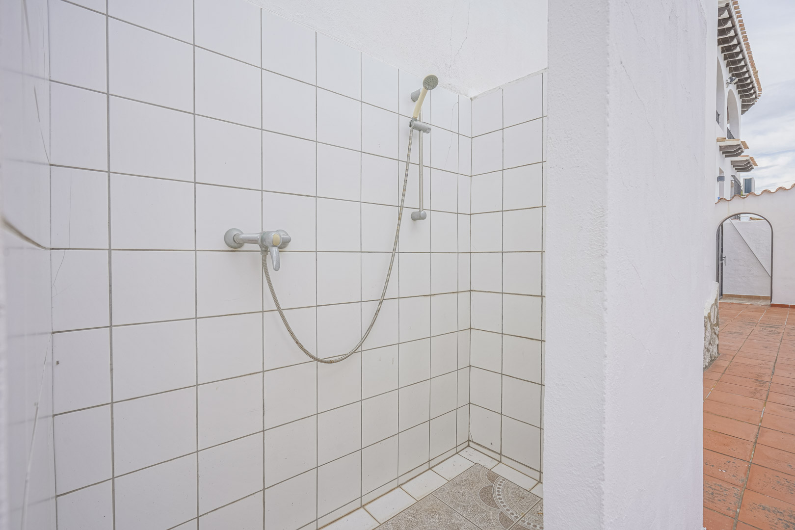 Ducha exterior con azulejos blancos y suelo decorativo en villa de Monte Pego.