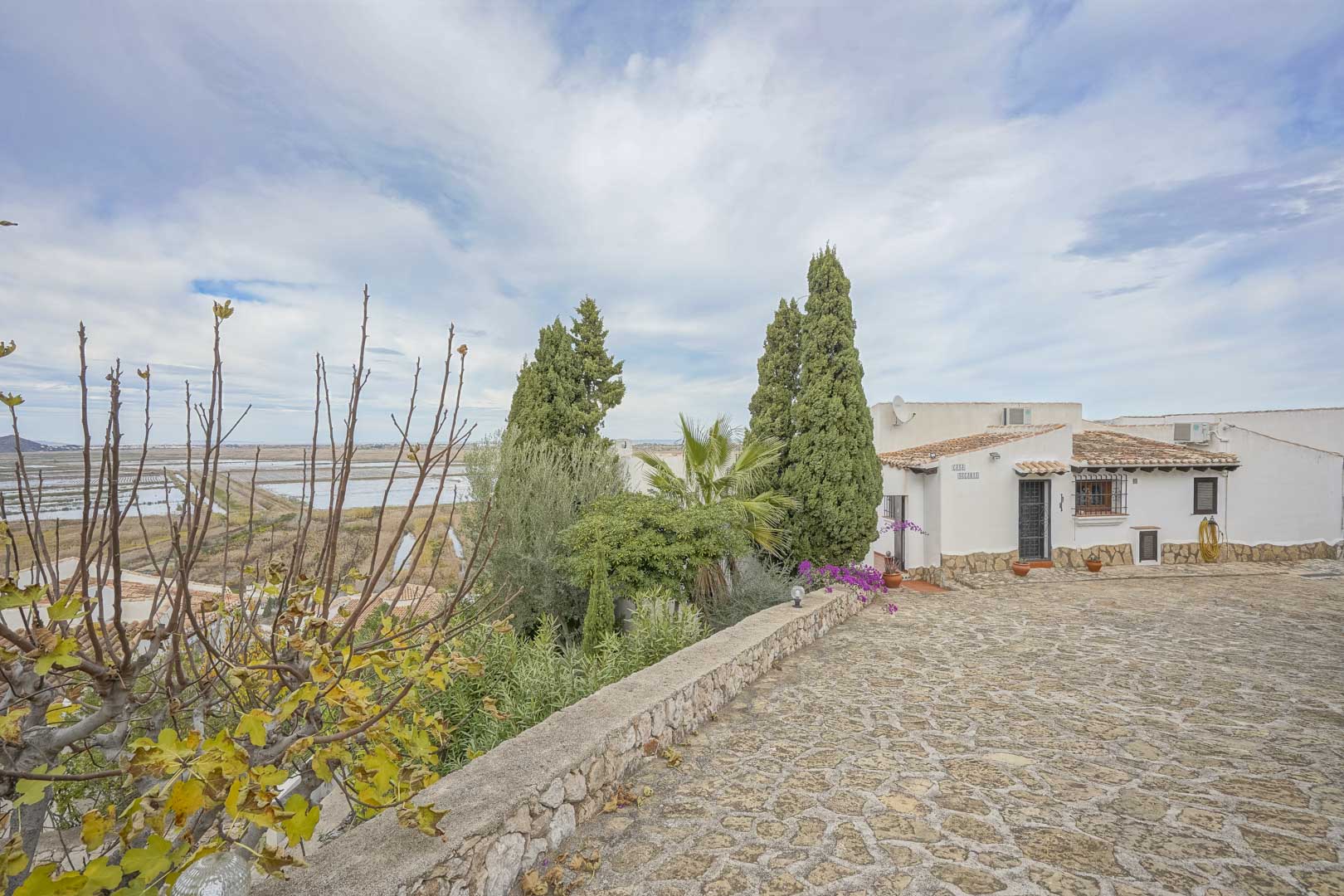 Vista exterior de la villa con entrada empedrada, jardín y vistas panorámicas de la reserva natural.