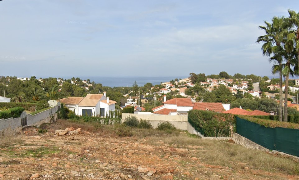Vista elevada de la urbanización con casas de tejas rojas y vistas al mar.