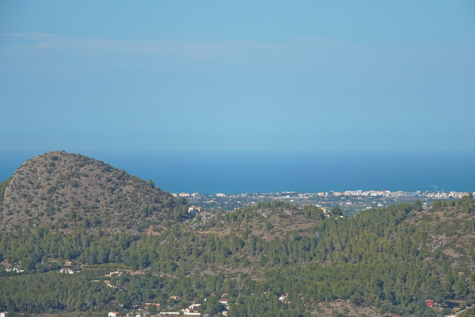 Vistas panorámicas desde la propiedad que abarcan montañas con vegetación mediterránea, el valle habitado y el mar Mediterráneo en el horizonte bajo un cielo despejado.