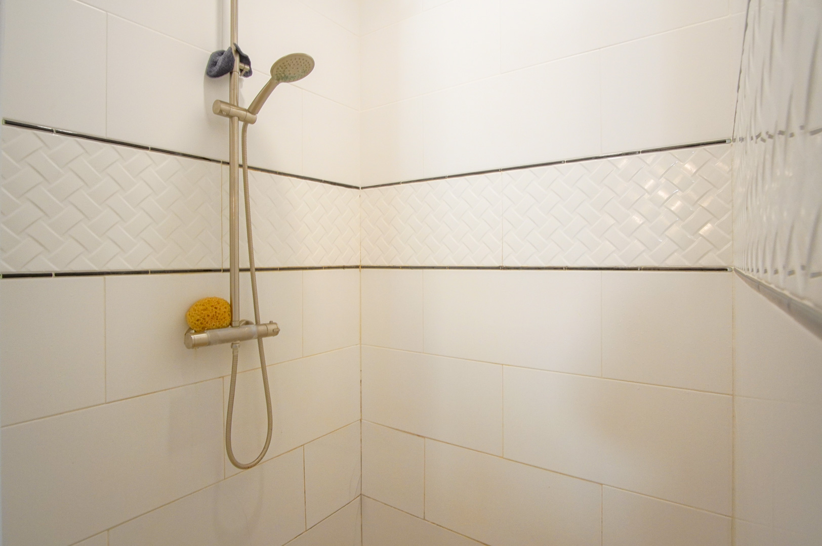 Ducha con revestimiento cerámico blanco, franja decorativa con relieve trenzado y grifería de acero inoxidable ajustable.