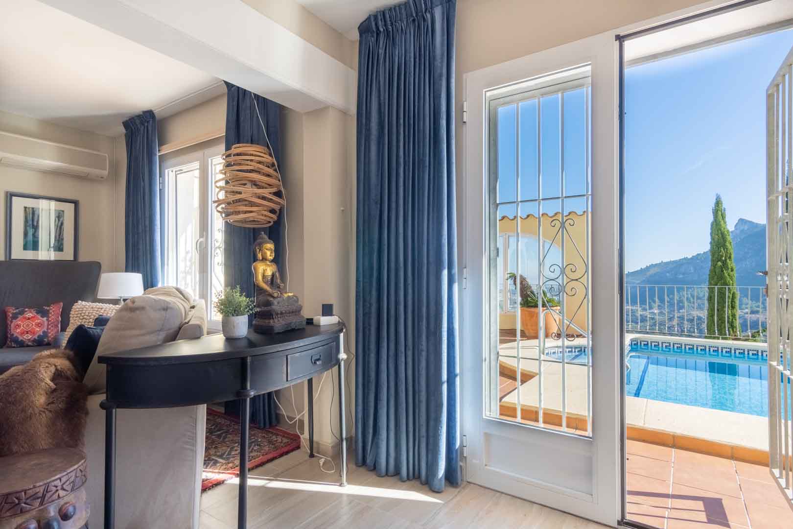 Salón con acceso directo a la terraza y piscina, decorado con cortinas azules y mobiliario auxiliar, ofreciendo vistas despejadas a la montaña.
