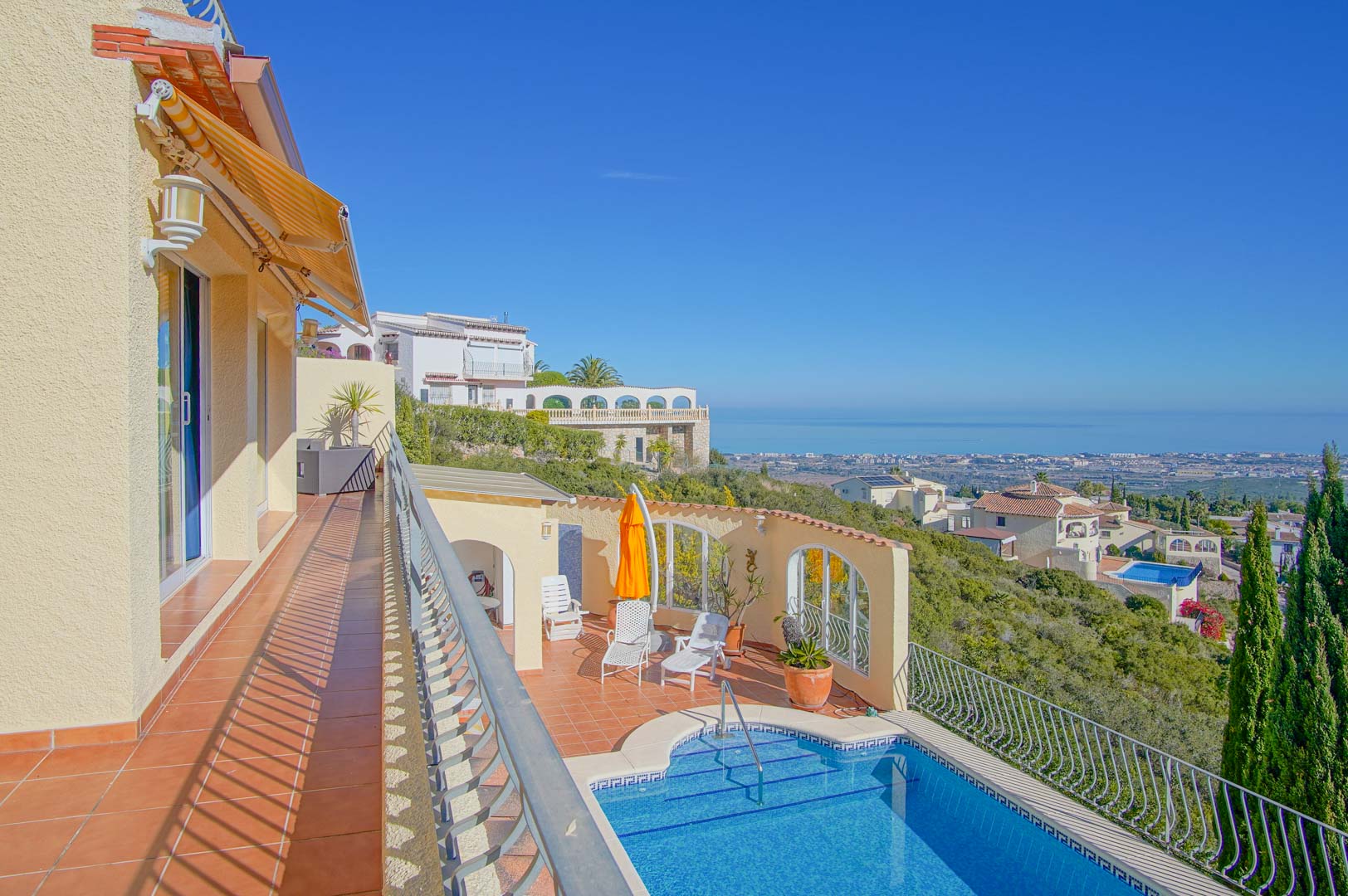 Terraza superior con suelos de terracota y toldo extensible, con vistas directas a la zona de piscina y una panorámica despejada del litoral mediterráneo.