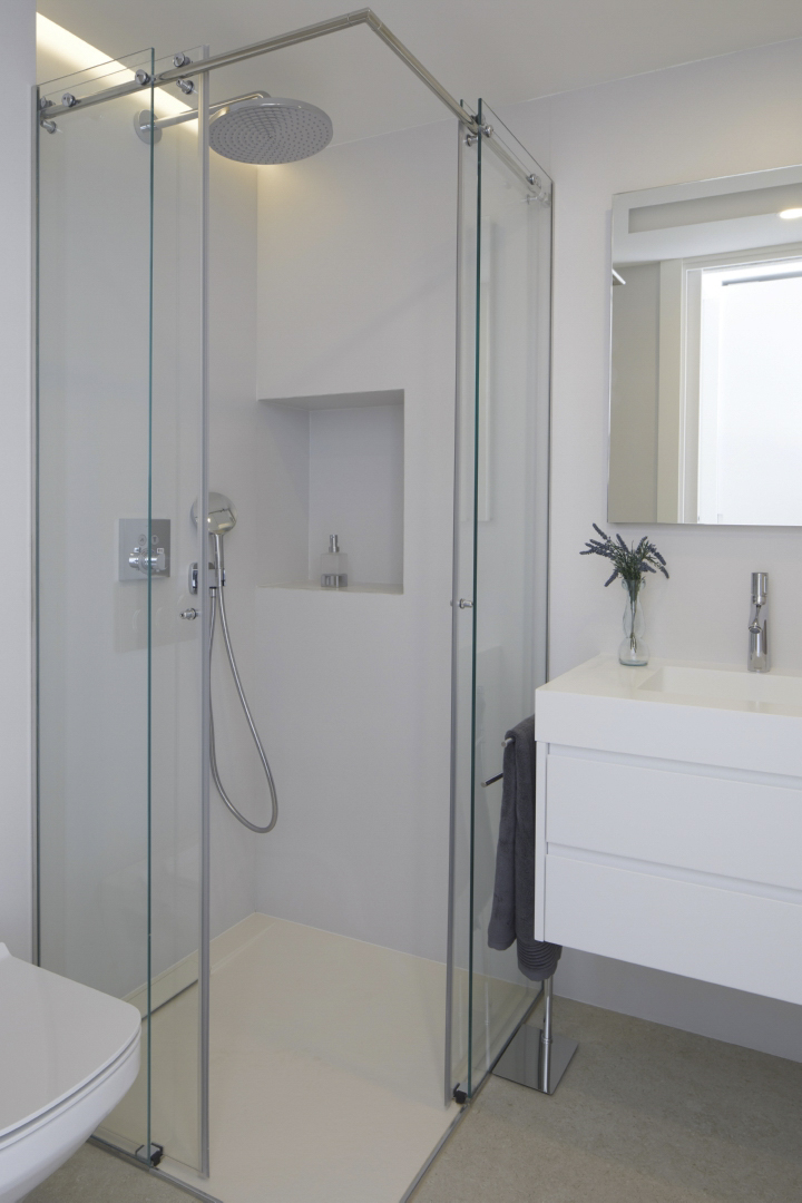 Baño moderno con cabina de ducha de vidrio, rociador de efecto lluvia y hornacina integrada. Incluye un mueble lavabo suspendido en blanco con grifería cromada y espejo rectangular.