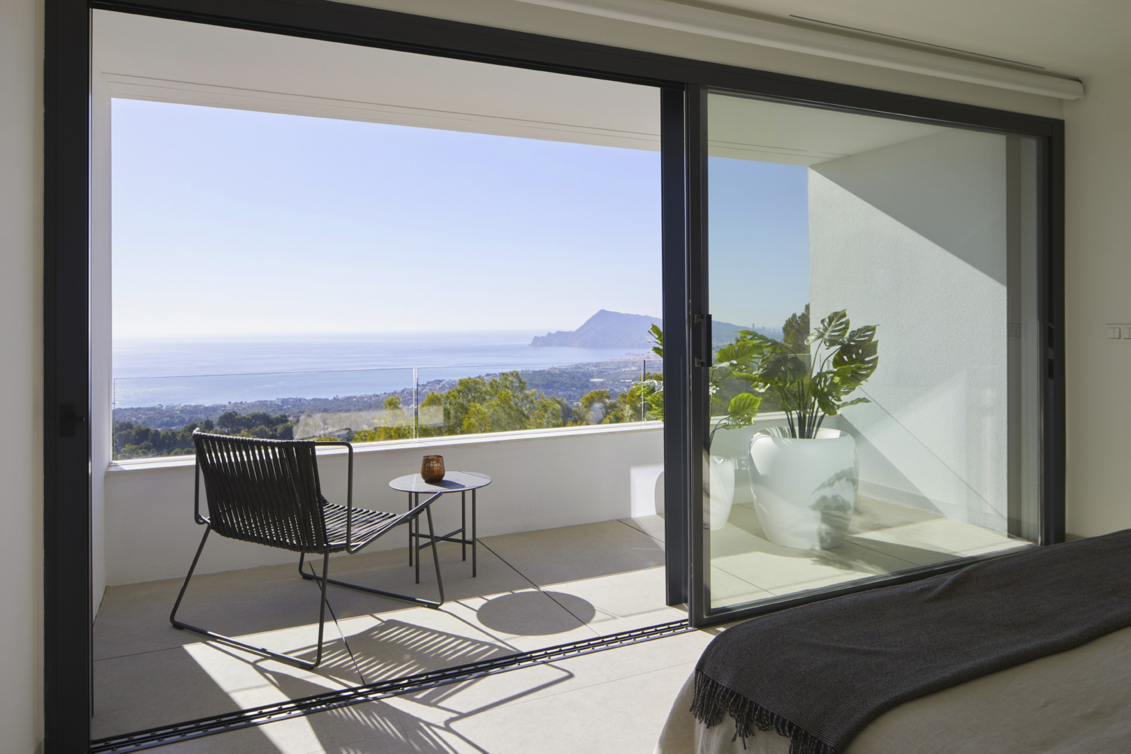 Dormitorio con acceso directo a terraza privada mediante ventanales correderos. Incluye vistas al mar, mobiliario exterior moderno y barandilla de cristal.