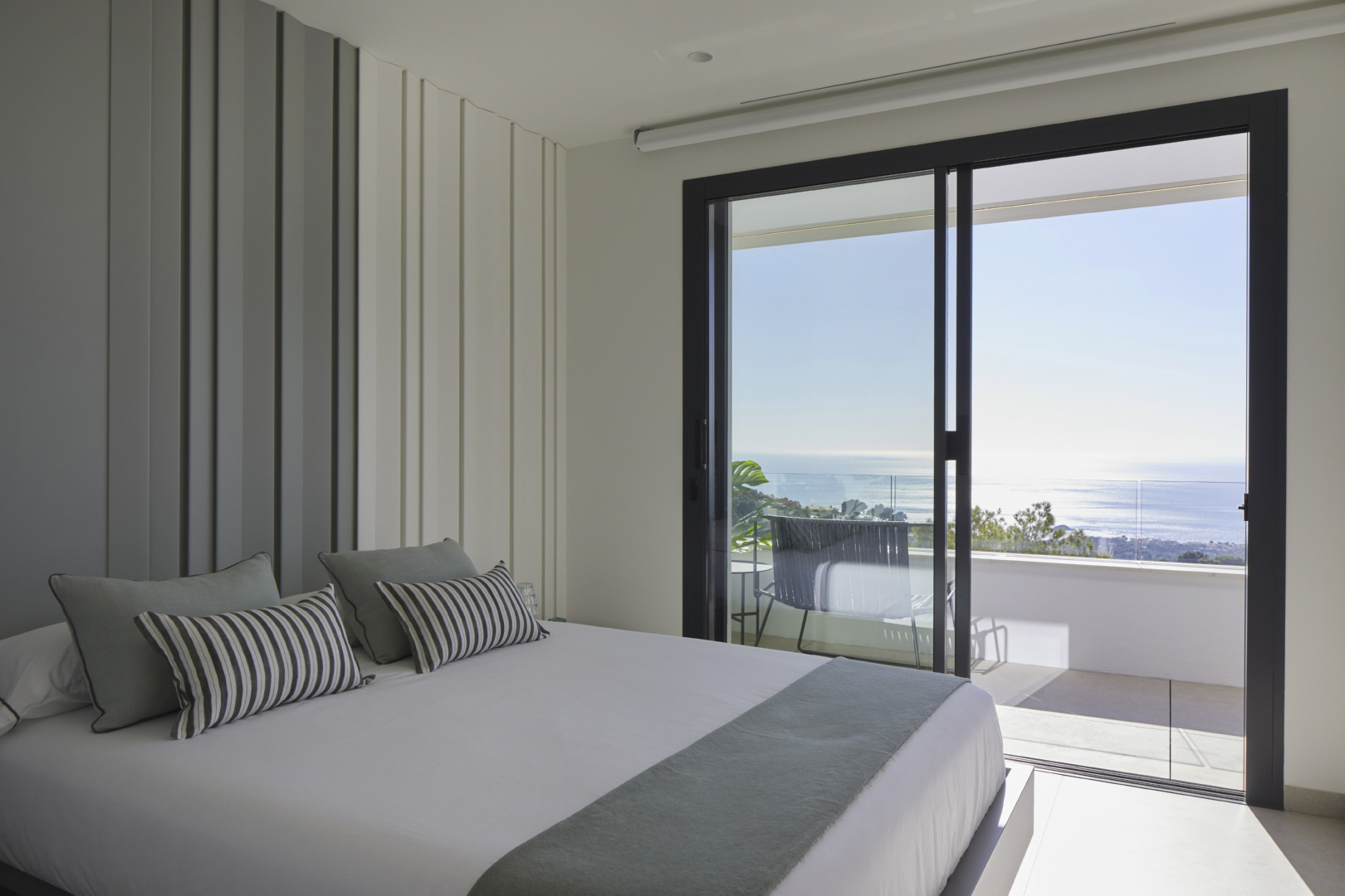 Dormitorio luminoso con panelado vertical decorativo y acceso directo a una terraza privada con vistas panorámicas al mar Mediterráneo.