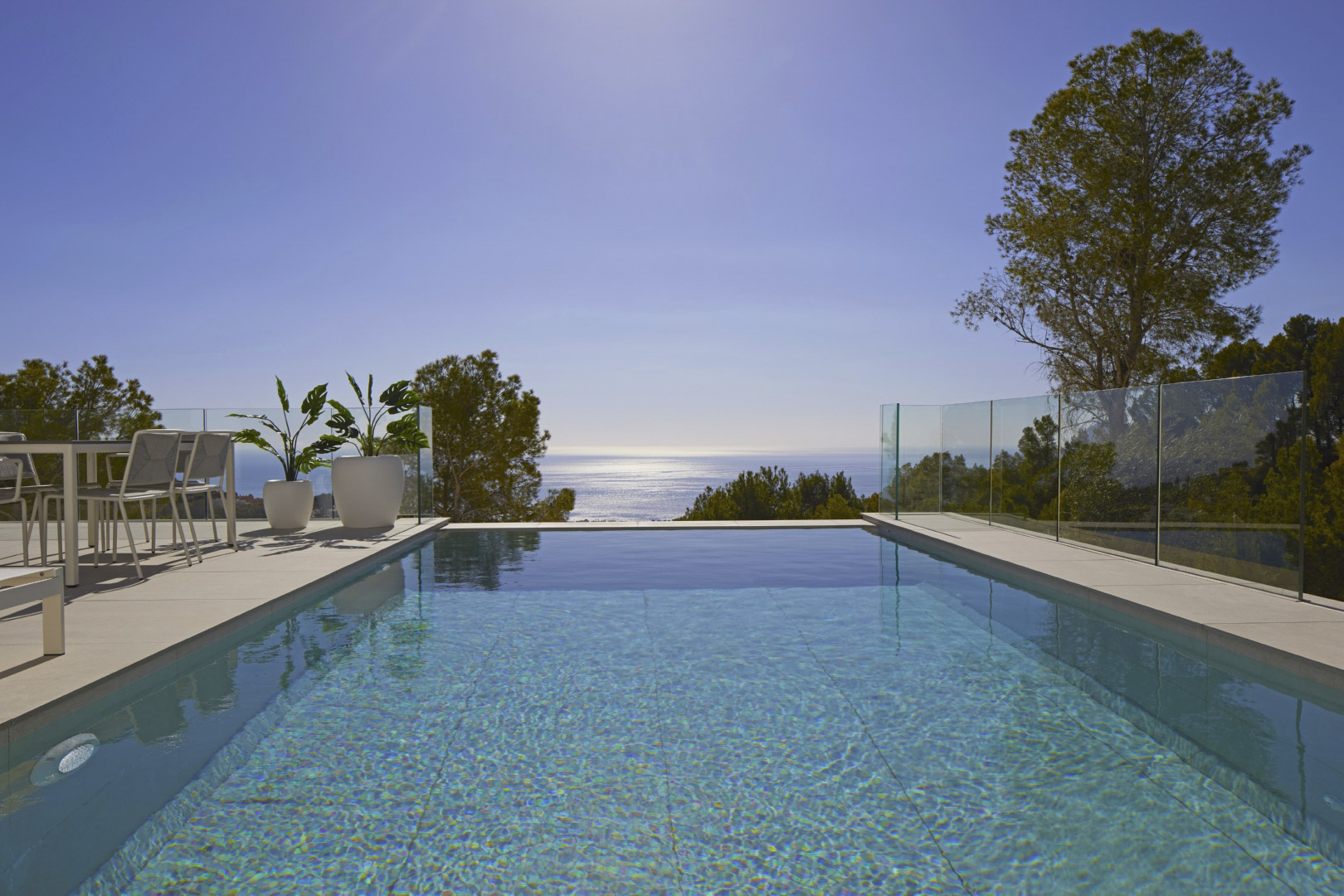 Piscina infinita con vistas panorámicas al mar Mediterráneo, rodeada por una terraza de gres porcelánico, mobiliario de exterior y barandillas de cristal.