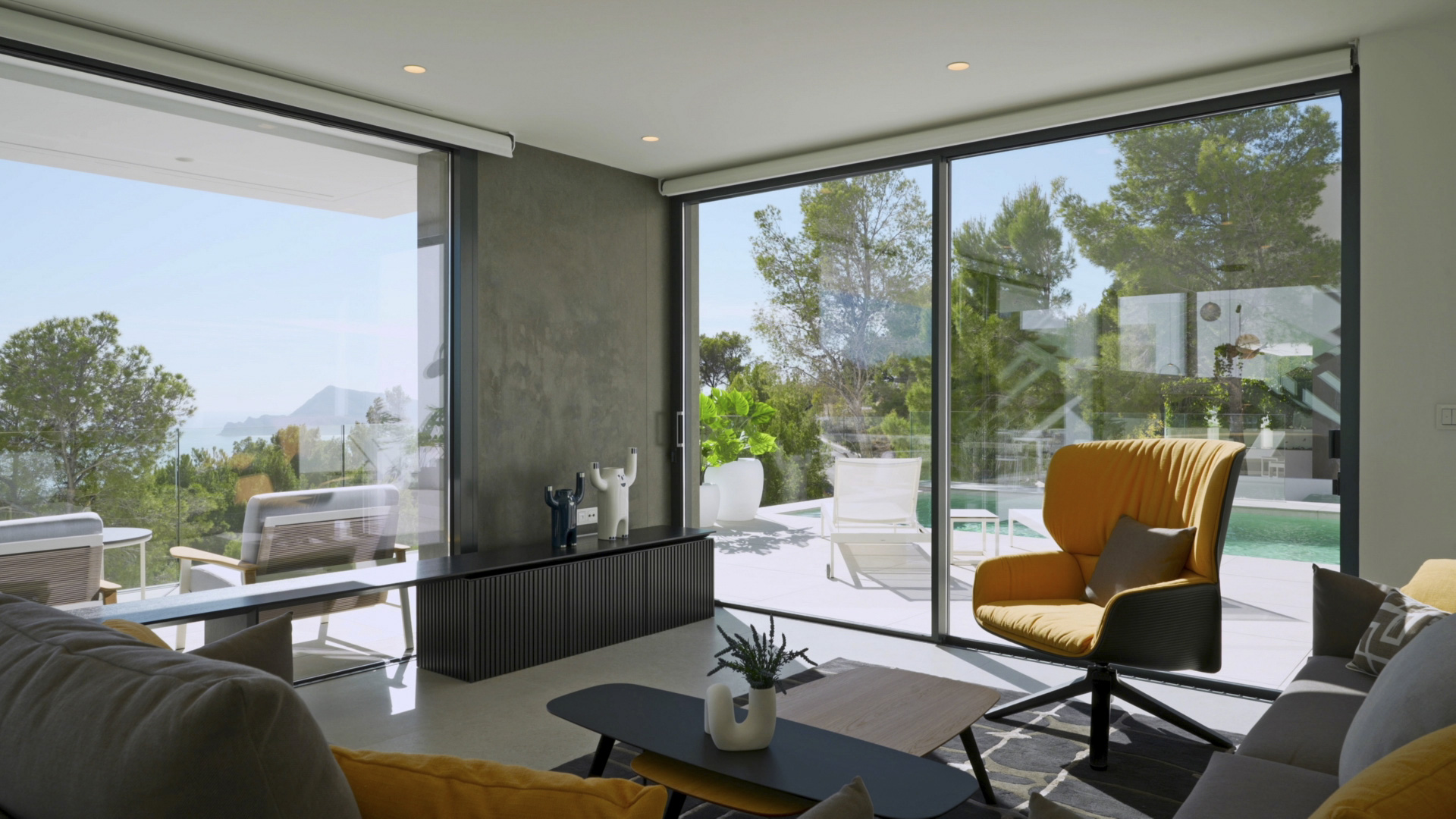 Salón luminoso con ventanales de suelo a techo, vistas al mar y a la piscina. Incluye mobiliario de diseño, sillón mostaza y acceso directo a la terraza exterior.