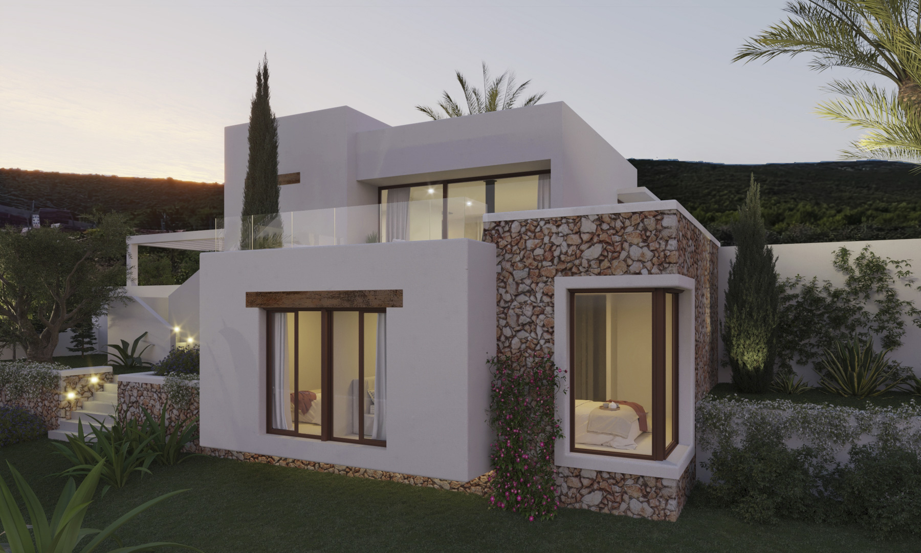 Fachada de estilo ibicenco con muros de piedra seca y volúmenes blancos, destacando sus amplios ventanales y un jardín mediterráneo iluminado al atardecer.