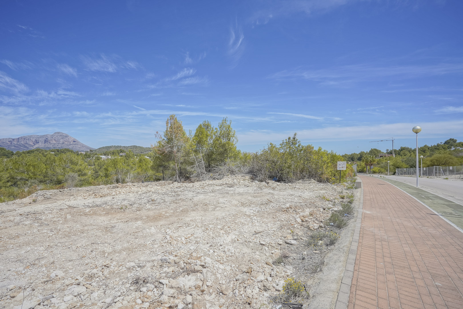 Parcela elevada de 1.000 m2 en Jávea, con terreno despejado y vistas directas al macizo del Montgó, situada junto a una zona residencial urbanizada con aceras.