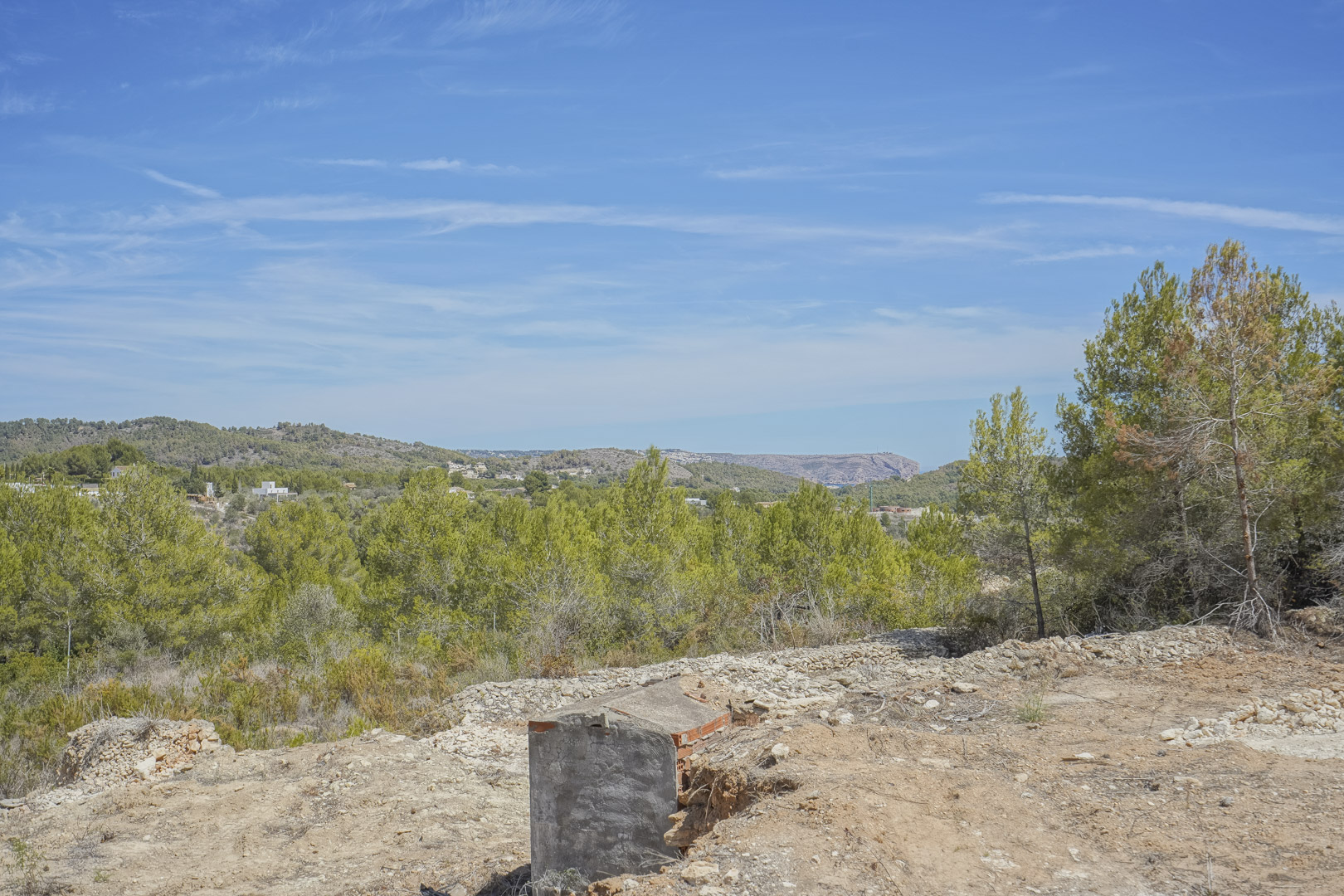 Vista panorámica desde la parcela elevada, destacando el entorno natural de pinos y el paisaje montañoso de Jávea bajo un cielo despejado.