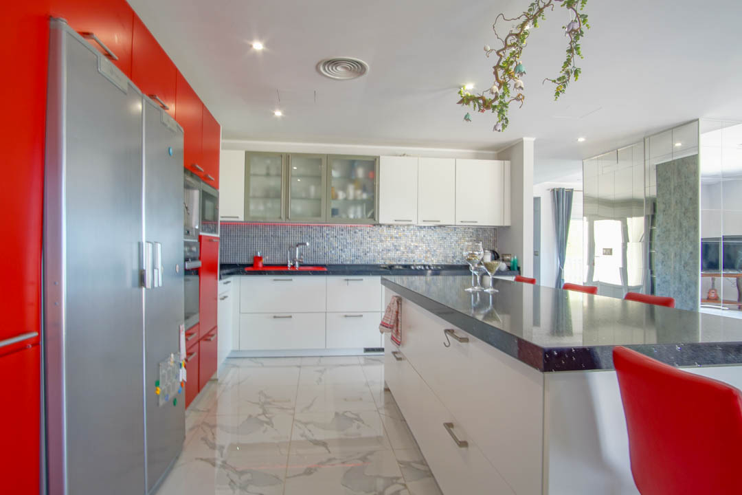Cocina de diseño contemporáneo con armarios en rojo vibrante y blanco, isla central con encimera oscura y suelos de gran formato con efecto mármol.