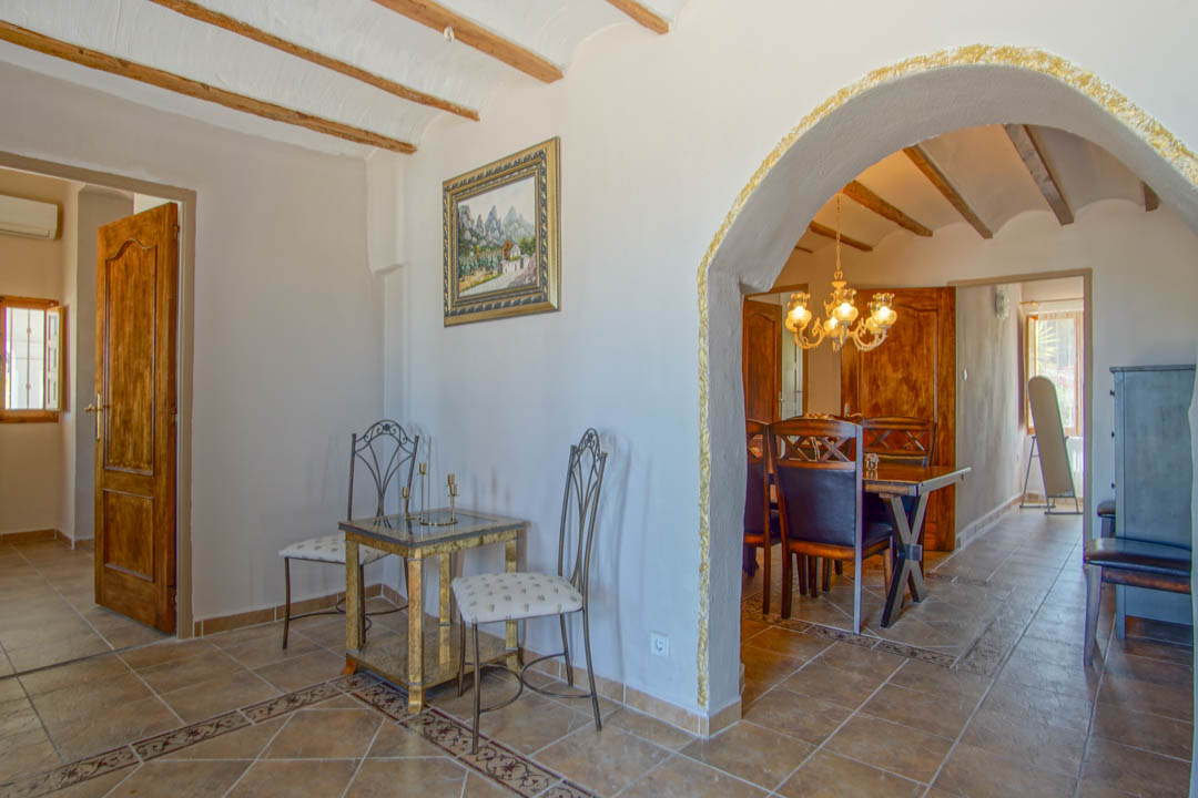 Distribuidor con techos de vigas de madera vista y suelos cerámicos decorados, conectado al comedor mediante un arco con detalles dorados.