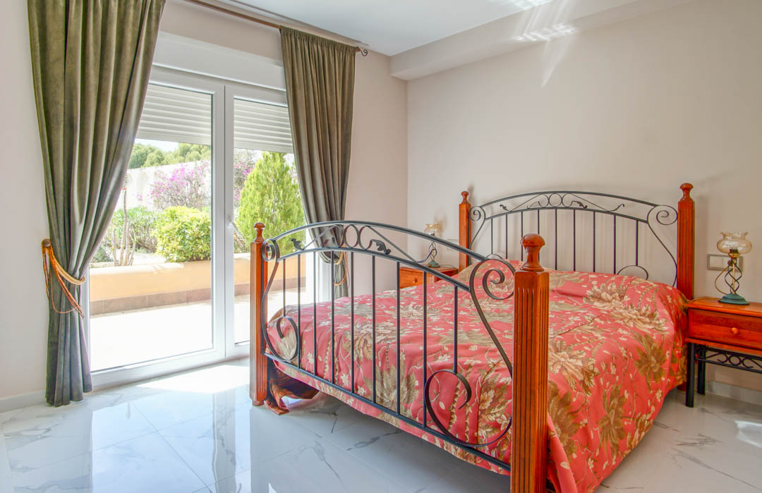Dormitorio con suelo de mármol pulido, cama de forja y madera, y acceso directo a la terraza mediante grandes ventanales que aportan luz natural.