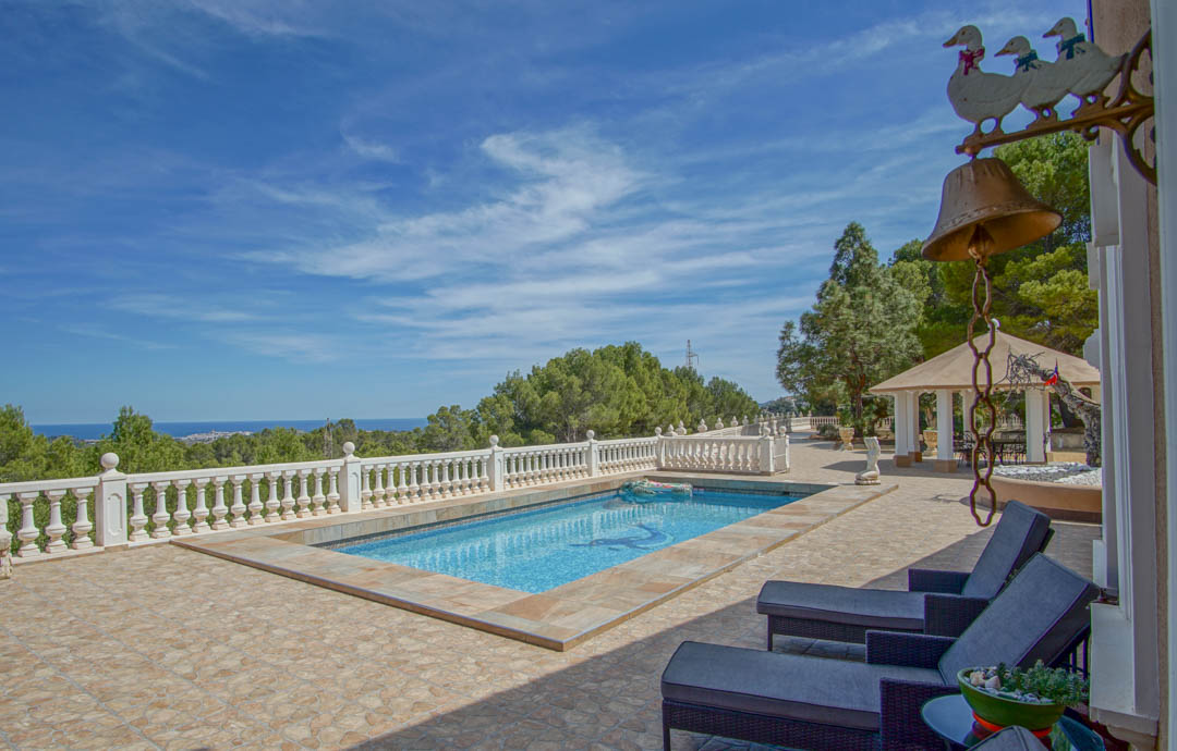 Terraza con piscina de mosaico y balaustrada blanca, ofreciendo vistas despejadas al mar y la costa de Altea bajo un cielo despejado.