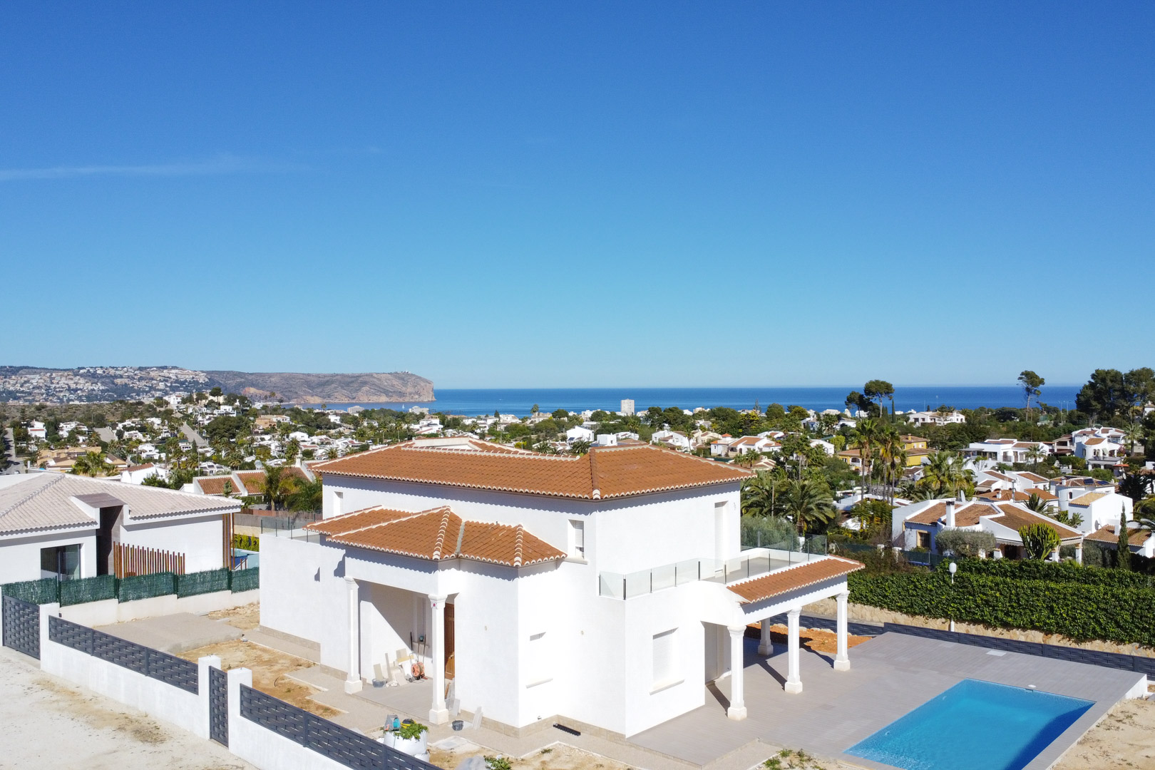 Vista aérea de la villa blanca con tejados de teja, piscina rectangular y amplias terrazas con barandillas de cristal que ofrecen vistas directas al mar Mediterráneo.