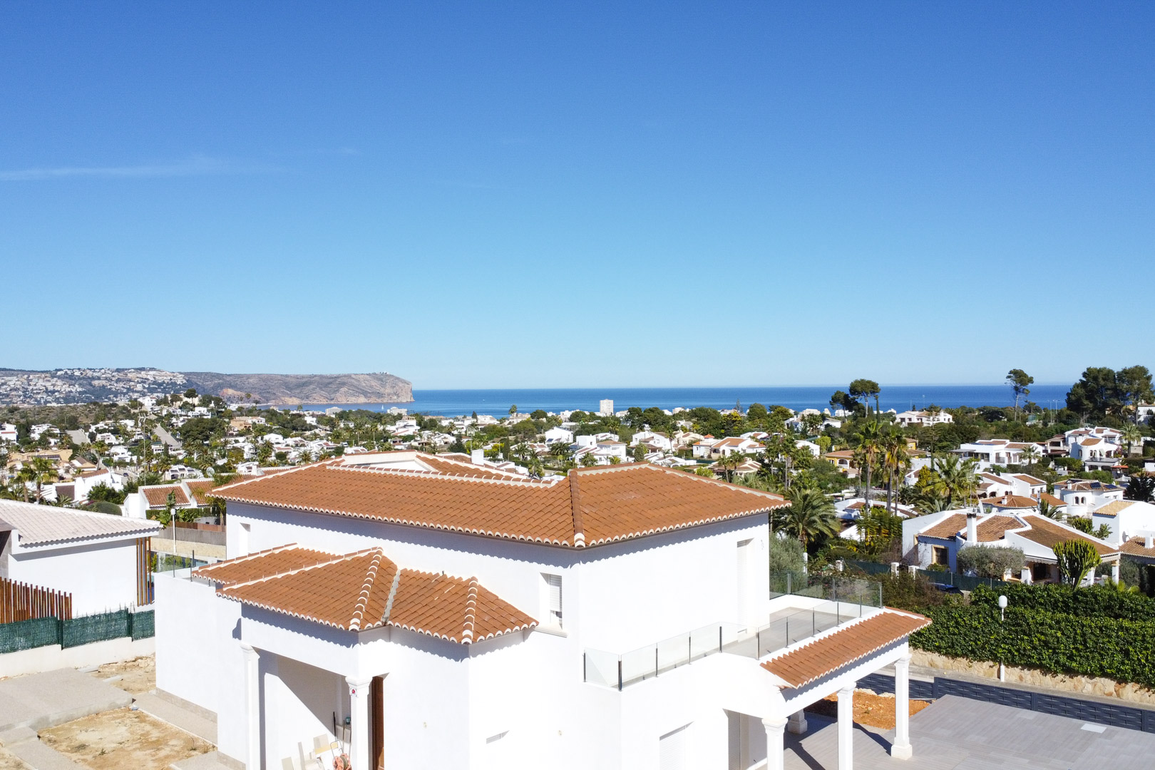 Vista exterior de la villa con tejados de teja y terrazas con barandillas de cristal, ofreciendo una panorámica despejada hacia el mar Mediterráneo en Jávea.
