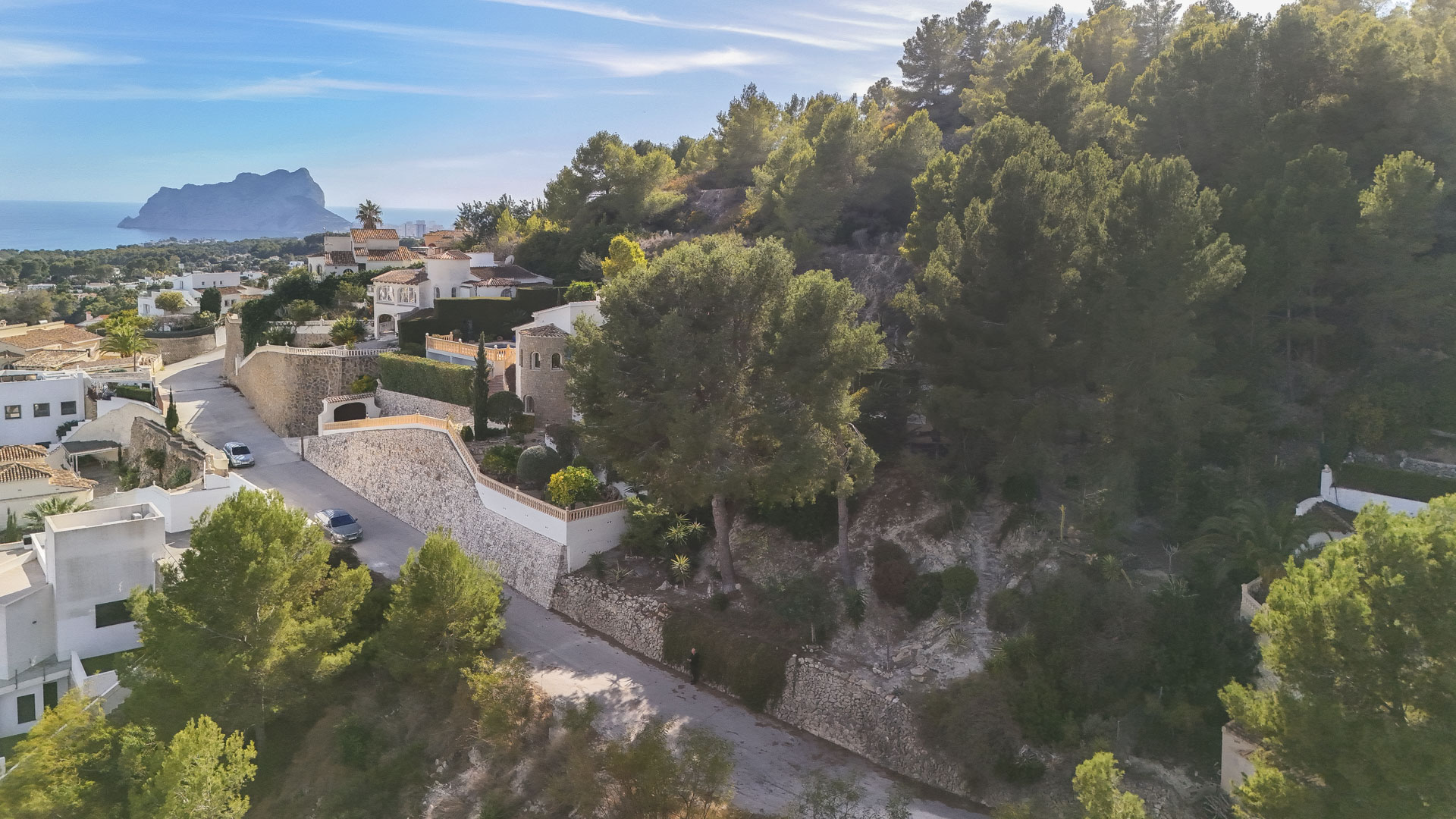 Vista aérea de la parcela elevada en Benissa, destacando su entorno natural de pinos y vistas despejadas al mar con el Peñón de Ifach al fondo.