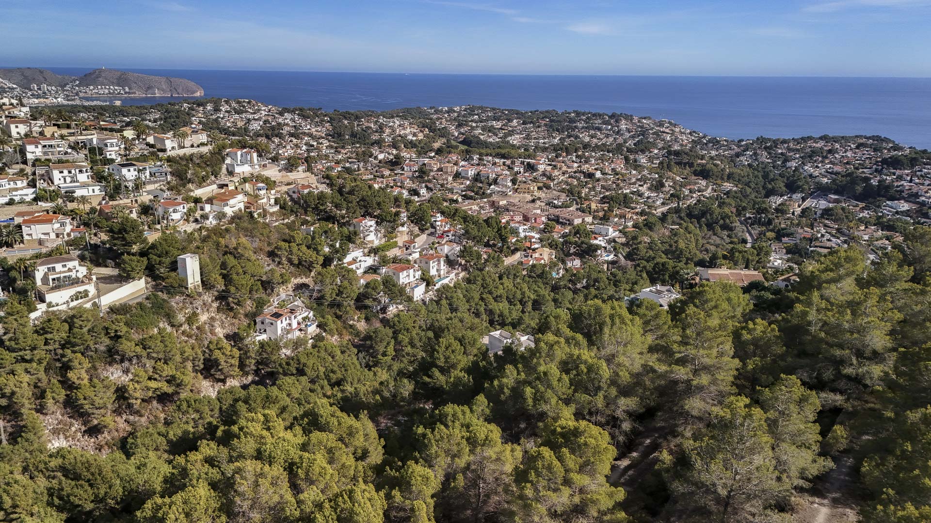 Vista aérea que muestra la integración de la zona residencial en el entorno natural de Benissa, con densos pinares y vistas panorámicas al mar Mediterráneo.