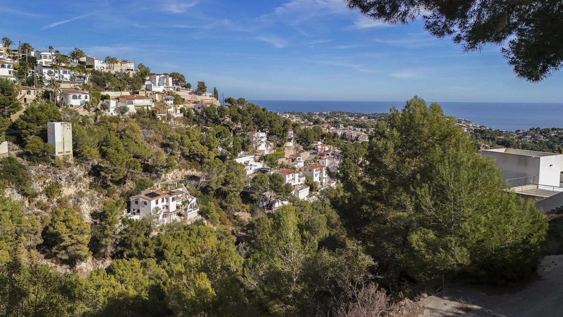 Vista panorámica desde la parcela elevada hacia el mar Mediterráneo, mostrando villas integradas en una ladera boscosa de pinos bajo un cielo despejado.