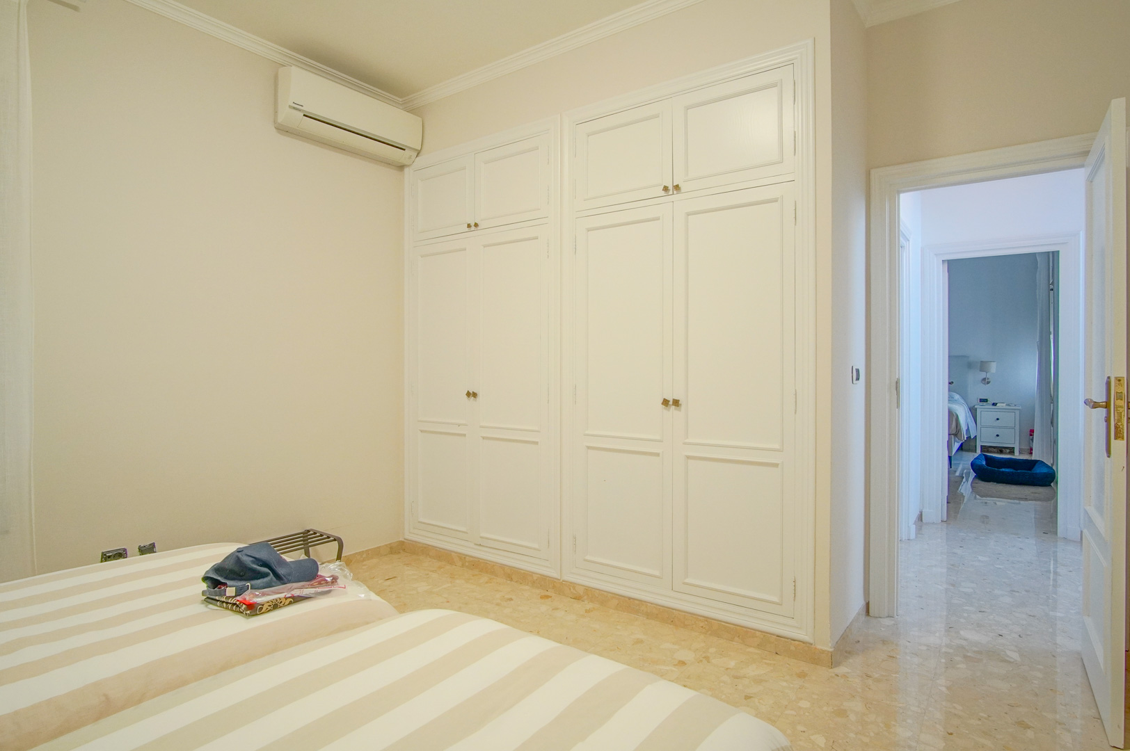Dormitorio con amplios armarios empotrados blancos, suelos de mármol y aire acondicionado individual, con acceso directo al pasillo de la vivienda.