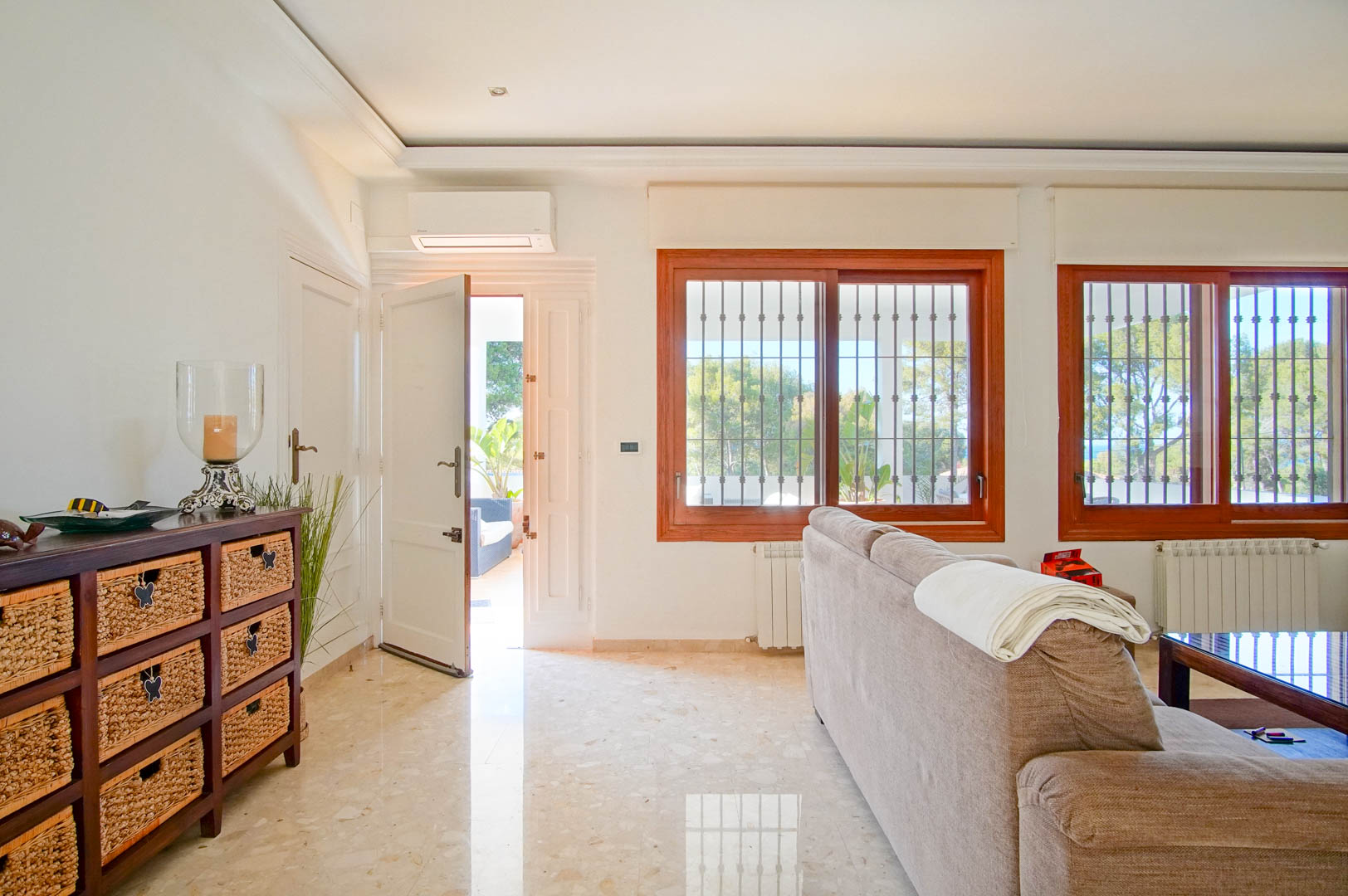 Salón luminoso con suelos de mármol pulido, ventanales de madera y acceso directo a la terraza. Dispone de aire acondicionado split y radiadores bajo las ventanas.