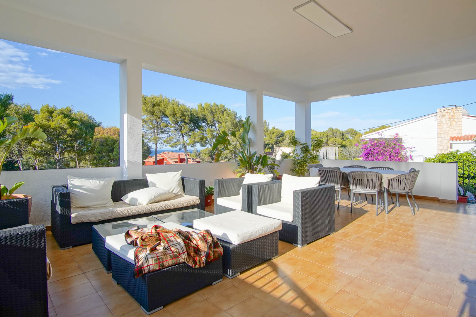 Terraza cubierta con mobiliario de ratán, comedor exterior y suelos cerámicos, ofreciendo vistas despejadas al entorno natural de Las Rotas y el mar.