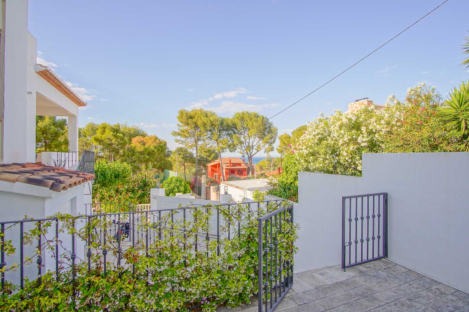 Vista desde la terraza con suelos de piedra y barandillas de forja, rodeada de vegetación mediterránea con vistas despejadas hacia el mar y el entorno arbolado de Las Rotas.