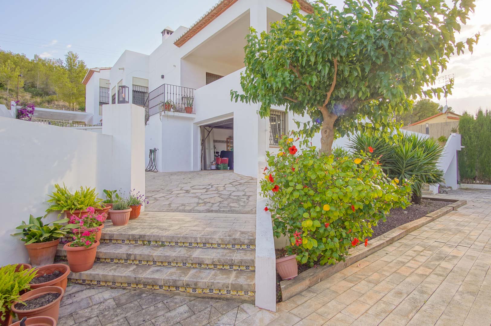 Vista exterior del acceso al garaje y semisótano, con escaleras de piedra decoradas con azulejos tradicionales y vegetación mediterránea.
