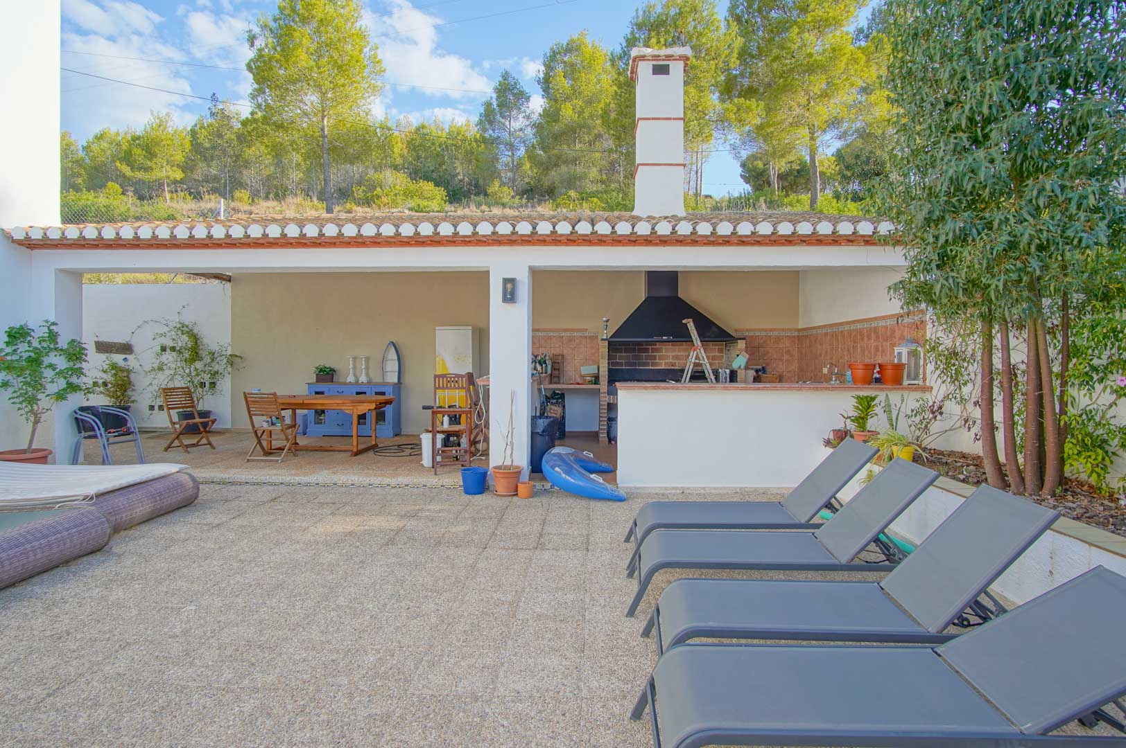 Zona de barbacoa cubierta con cocina exterior, comedor y terraza de piedra con tumbonas, integrada en el entorno boscoso del Parque Natural del Montgó.