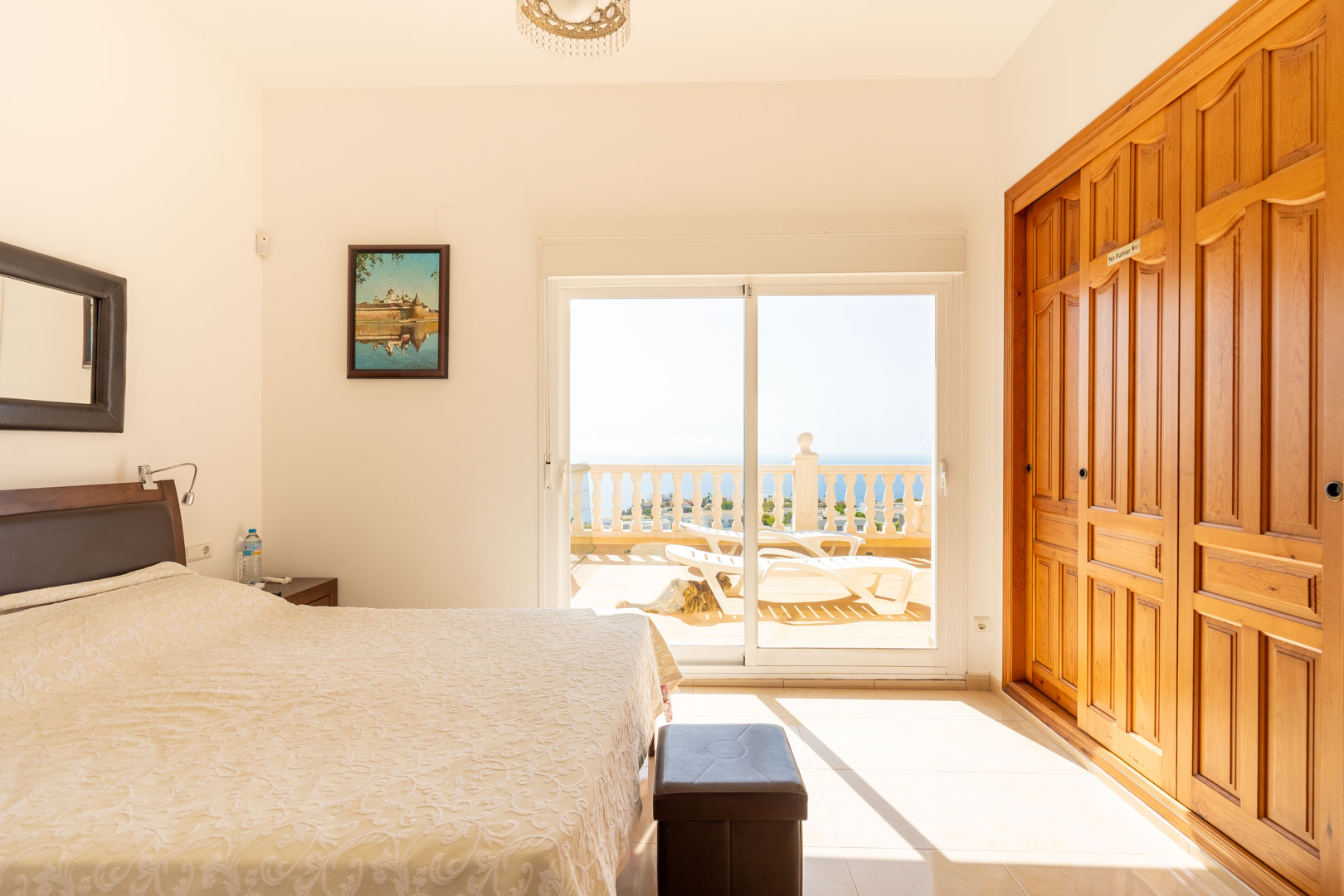Dormitorio con armarios empotrados de madera y acceso directo a una terraza soleada con vistas al mar a través de puertas correderas.