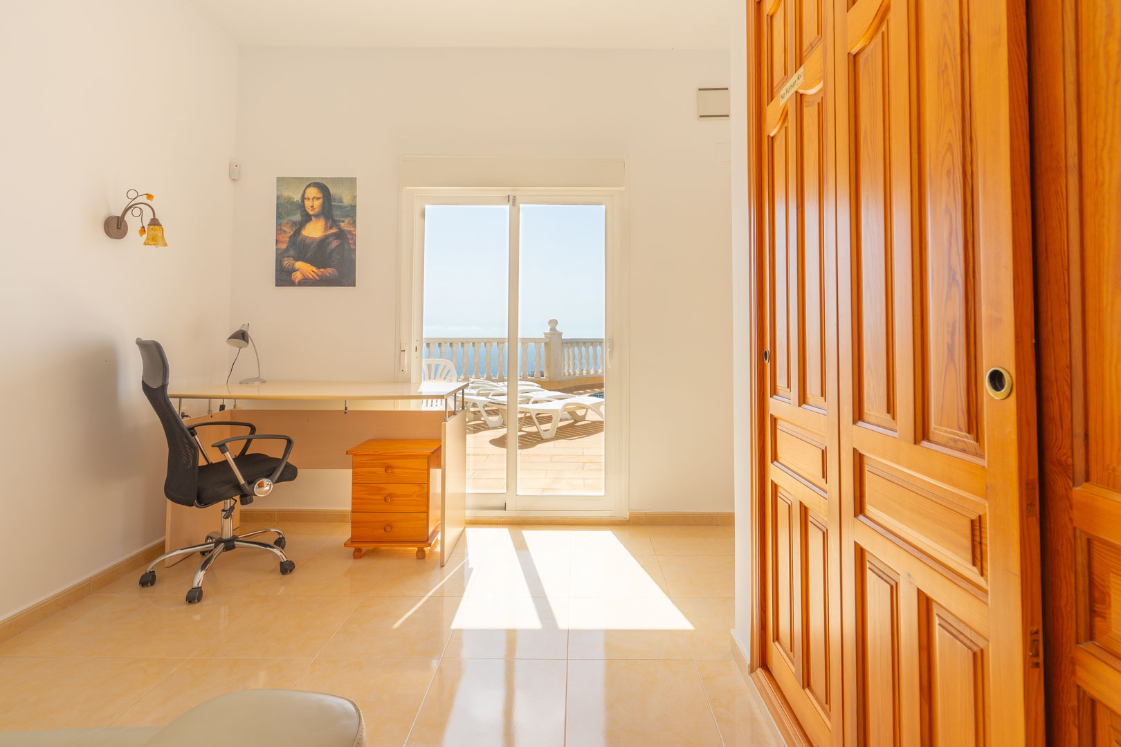 Habitación polivalente con escritorio, armarios empotrados de madera natural y acceso directo a la terraza con vistas al mar a través de puertas correderas.