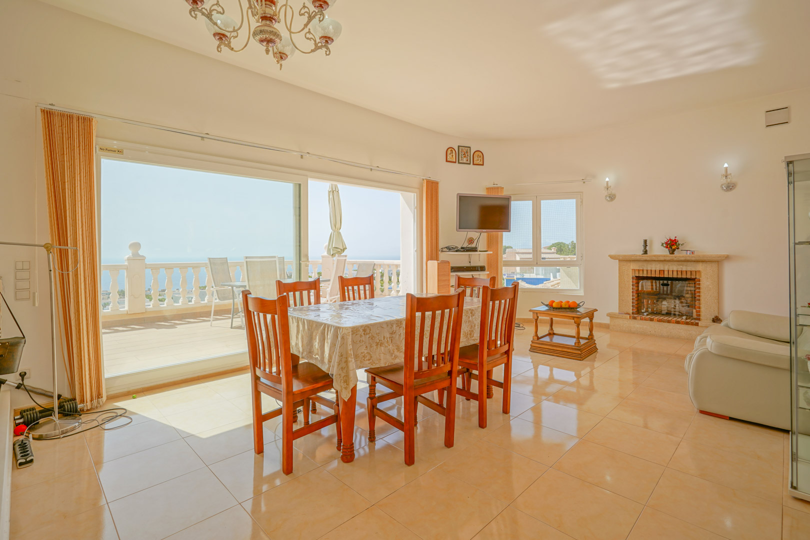Salón-comedor luminoso con chimenea de piedra, suelos cerámicos y acceso directo a la terraza mediante amplios ventanales con vistas al mar Mediterráneo.