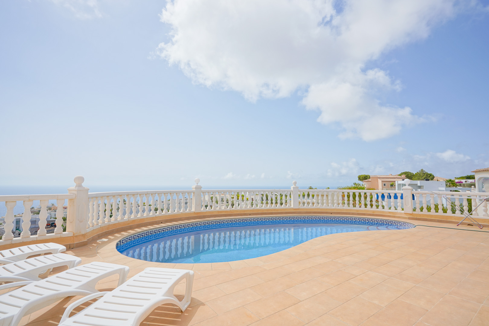 Terraza con piscina curva y balaustrada blanca, con vistas panorámicas al mar Mediterráneo y tumbonas sobre suelo de terracota.