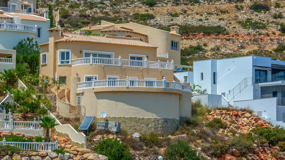 Vista exterior de la villa de estilo mediterráneo con fachadas en tono ocre, destacando sus amplias terrazas curvas con balaustradas blancas integradas en la ladera.