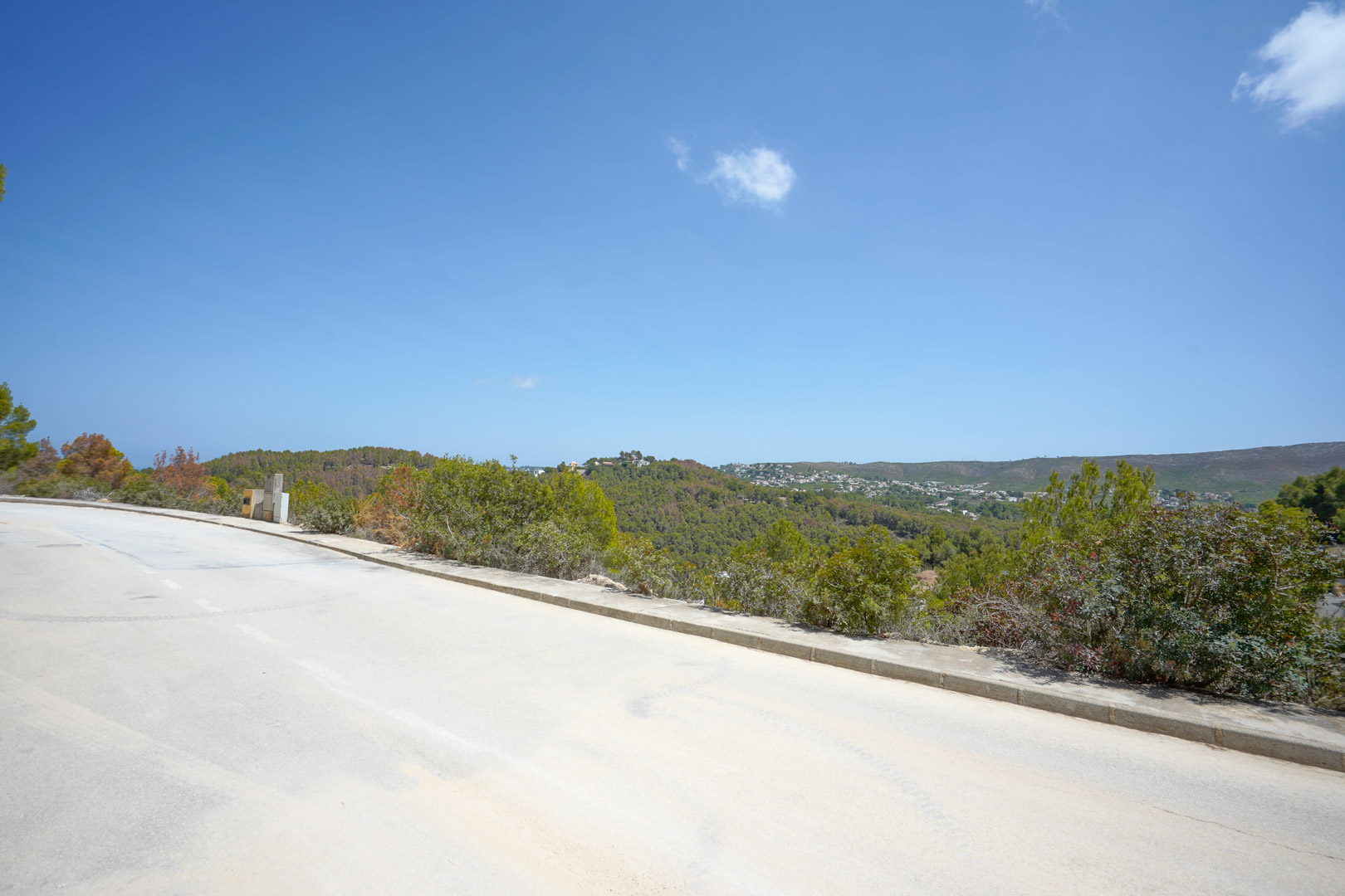 Vista panorámica desde la calle asfaltada de la urbanización, mostrando la infraestructura de servicios y las vistas despejadas hacia las colinas boscosas.