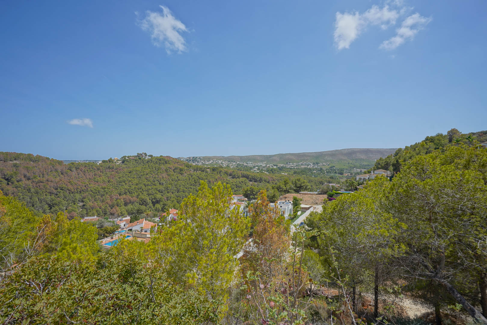Vista panorámica desde la parcela elevada hacia el valle boscoso, con viviendas residenciales y el horizonte del mar Mediterráneo al fondo.