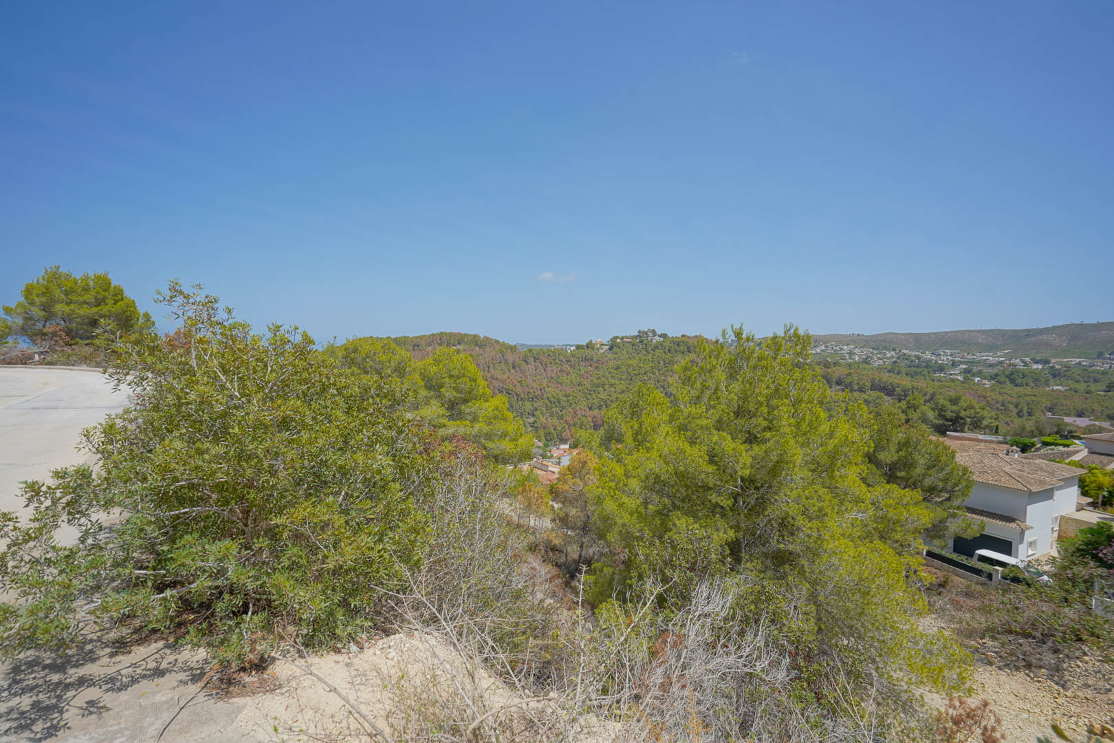 Vista panorámica desde la parcela elevada que muestra la infraestructura vial pavimentada y el entorno natural de colinas mediterráneas.