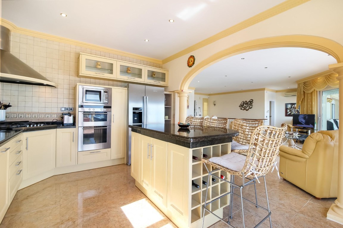 Cocina de concepto abierto con isla de granito oscuro, electrodomésticos de acero inoxidable y un arco decorativo que conecta con el salón principal.