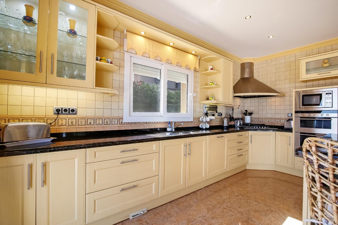 Cocina de estilo tradicional con mobiliario en tono crema, encimera de granito oscuro y electrodomésticos integrados de acero inoxidable bajo iluminación empotrada.
