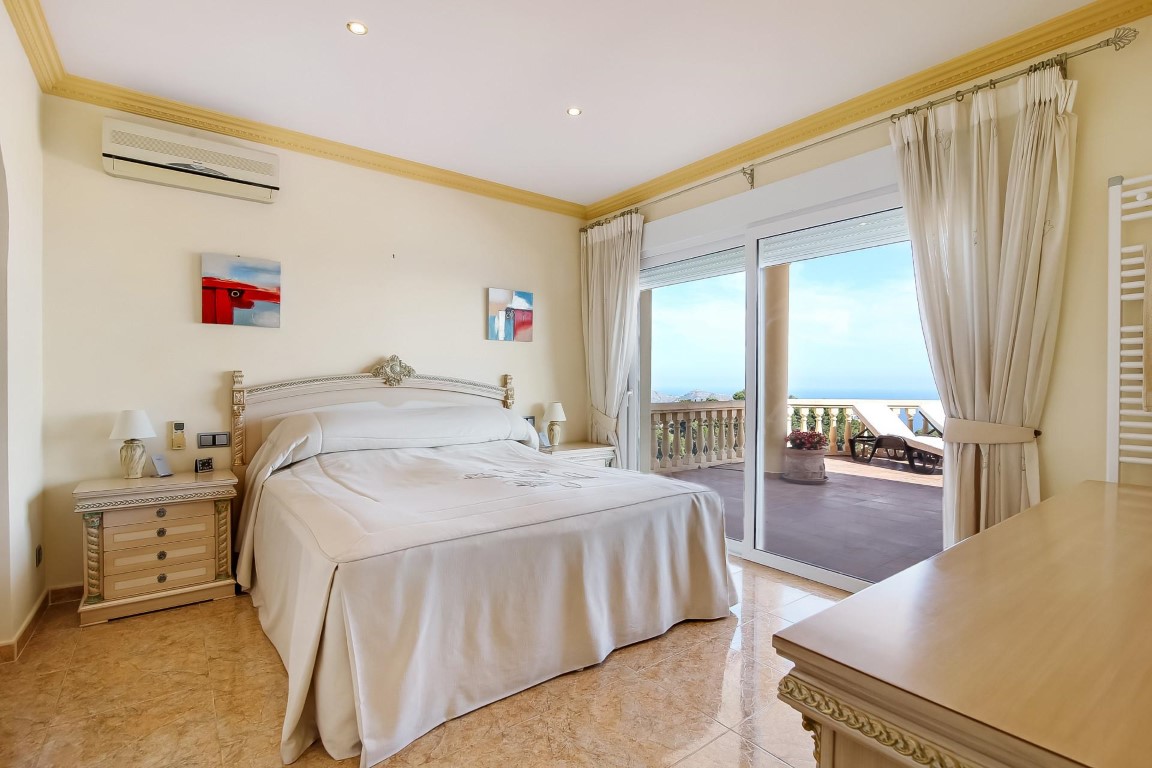 Dormitorio principal con acceso a terraza privada, suelos de gres, aire acondicionado y amplios ventanales con vistas despejadas al mar Mediterráneo.