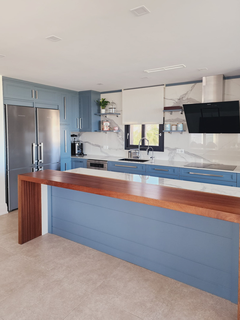 Cocina moderna con armarios azules, encimera de efecto mármol y barra de madera maciza. Dispone de electrodomésticos integrados y una amplia zona de trabajo luminosa.
