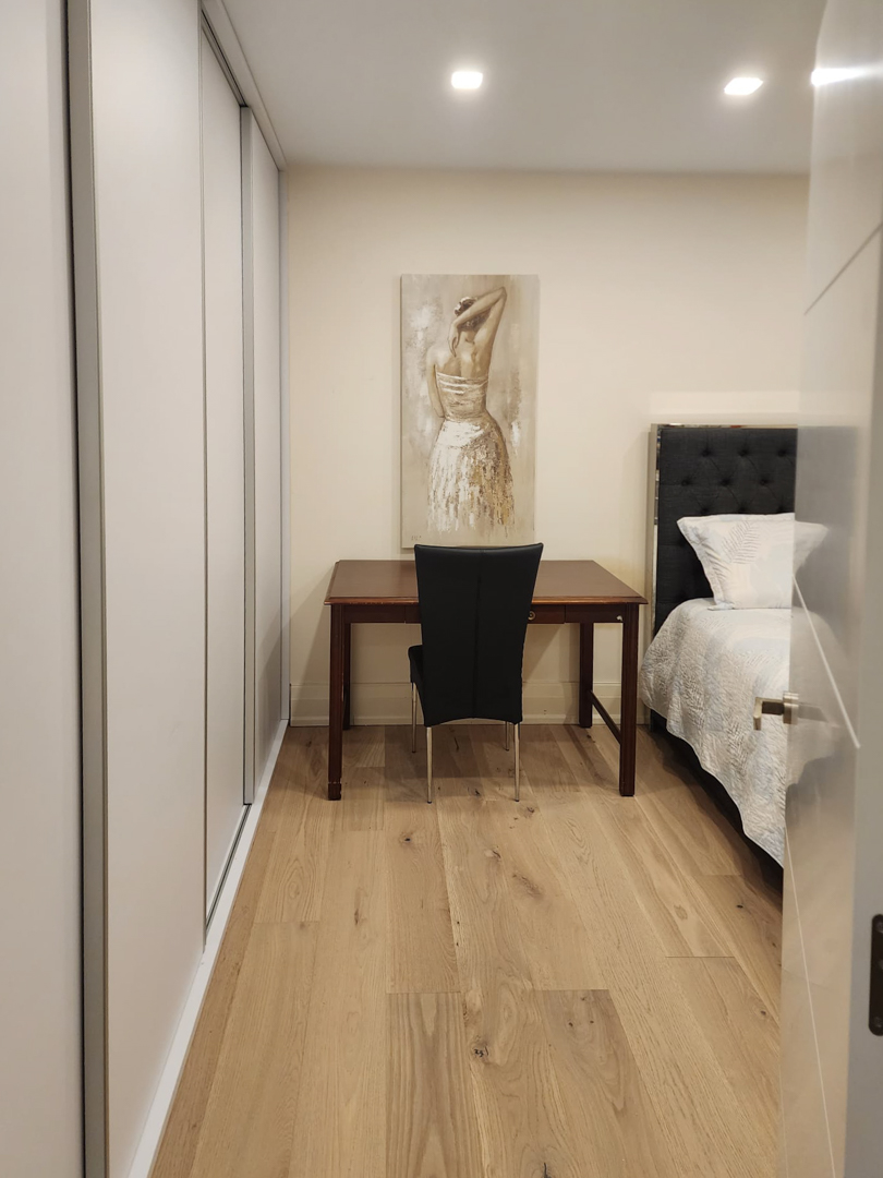Dormitorio con armarios empotrados de suelo a techo, zona de escritorio en madera noble y suelos de tarima de roble bajo iluminación empotrada.