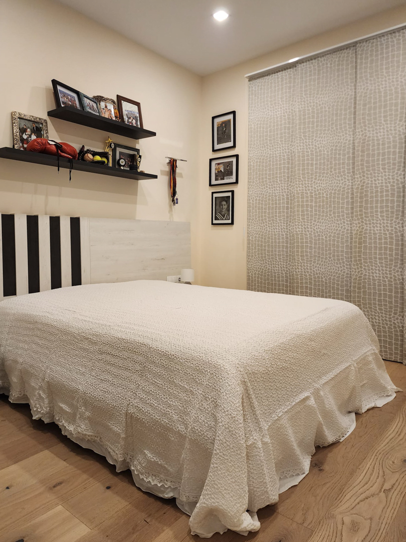 Dormitorio con suelo de madera de roble, cabecero de diseño y estanterías flotantes. Incluye cortinas de panel con estampado y luz cenital empotrada.