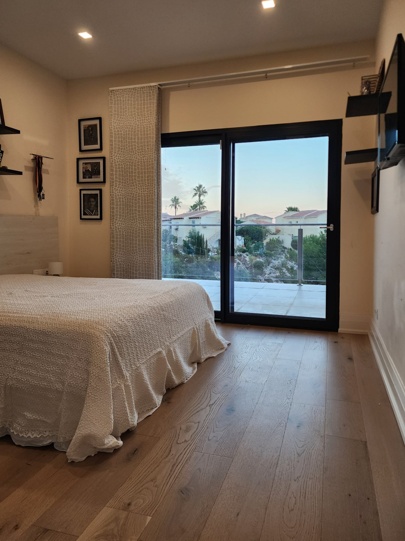 Dormitorio con suelos de madera, iluminación empotrada y acceso directo a una terraza privada a través de grandes ventanales correderos con vistas al entorno.