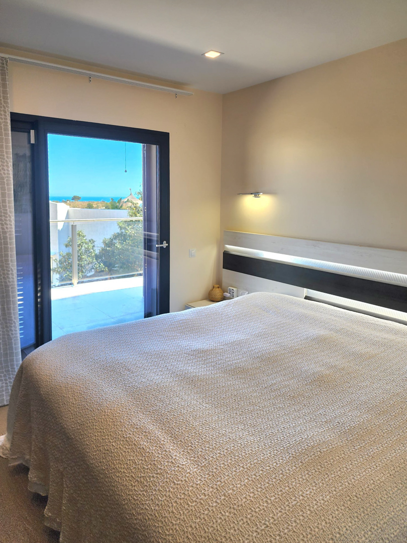 Dormitorio luminoso con cabecero integrado de iluminación LED y acceso directo a la terraza con vistas panorámicas al mar Mediterráneo.